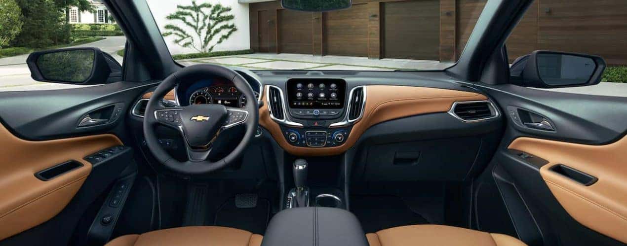 The tan and black interior of a 2021 Chevy Equinox shows the steering wheel and infotainment screen.