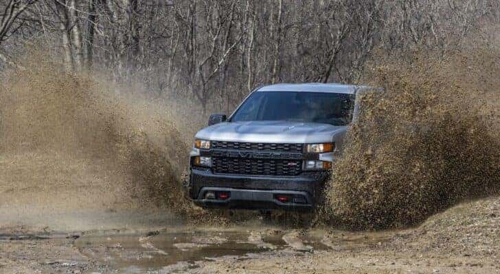 A grey 2020 Chevy Silverado 1500 Trail Boss is shown from the front at an angle while driving through mud after leaving a dealer that has a Chevy Silverado 1500 for sale.