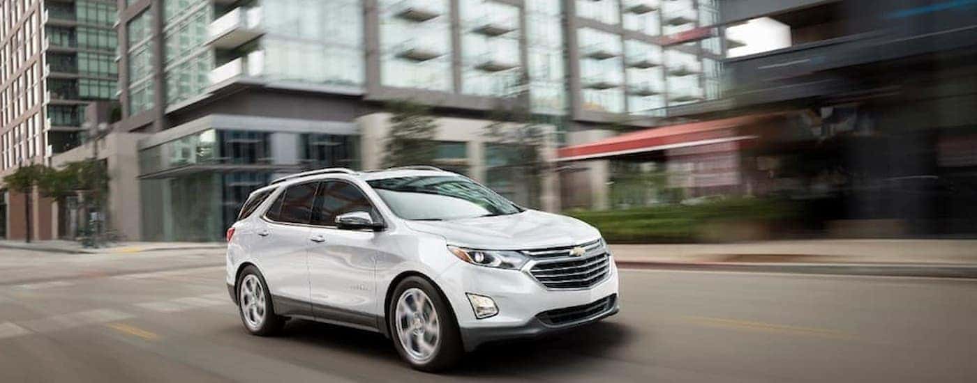 A white 2018 Chevy Equinox for sale is shown driving on a city street.