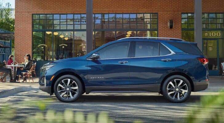 A blue 2023 Chevy Equinox Premier is shown from the side parked at a crosswalk.