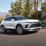 A white 2024 Chevy Blazer 3LT is shown driving on a hill through a town.