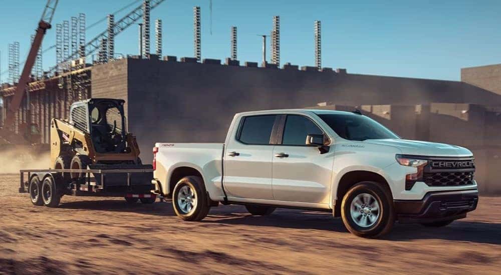A white 2024 Chevy Silverado 1500 WT is shown towing a trailer.