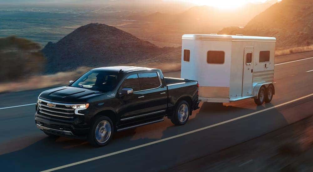 Overhead view of a black 2024 Chevy Silverado 1500 High Country towing a trailer on a coastal highway.
