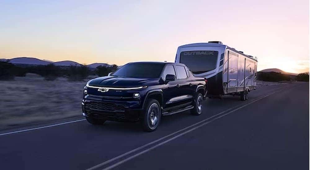 A black 2025 Chevy Silverado EV RST is shown towing a trailer on a highway.