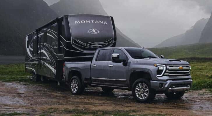 A grey 2024 Chevy Silverado 2500 High Country towing a trailer through mud.