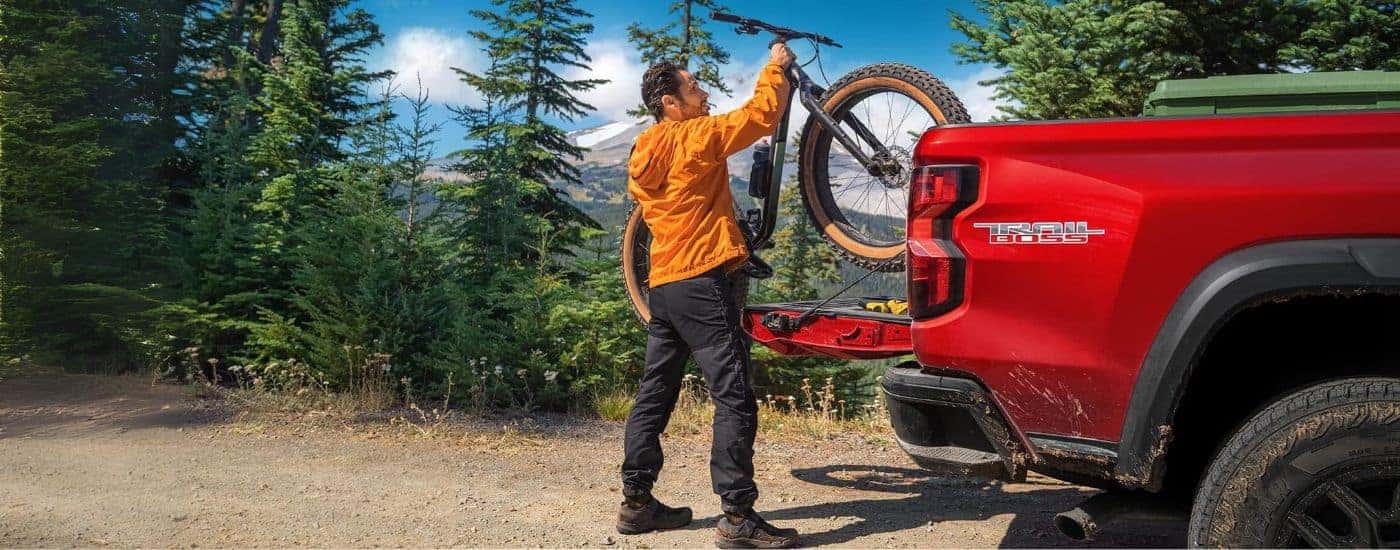 A person is shown loading a bike into a red 2023 Chevy Colorado Trail Boss.