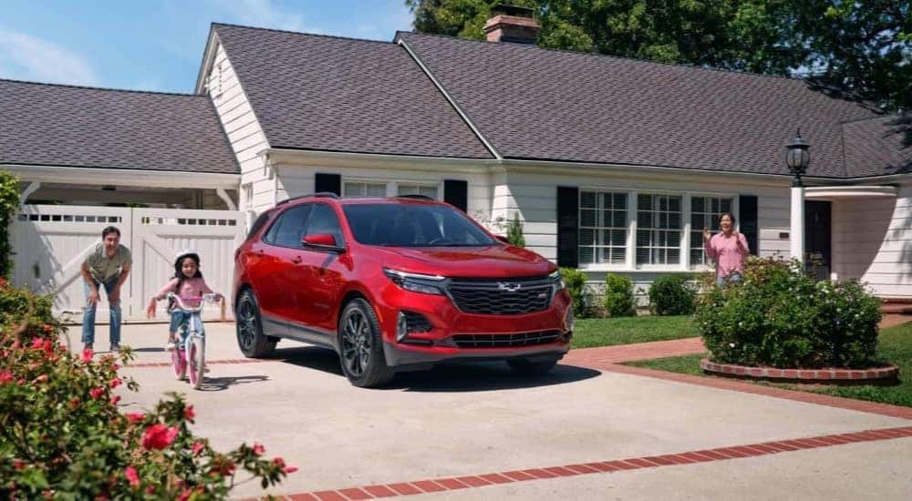 A red 2024 Chevy Equinox RS parked in the driveway of a suburban home.