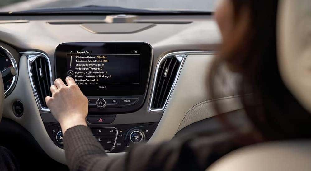 A person is shown viewing the teen driver safety report card on an infotainment screen in a Chevy vehicle.