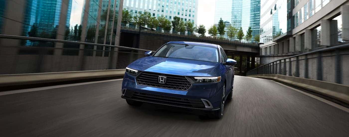 A blue 2023 Honda Accord Touring Hybrid crossing a city bridge.