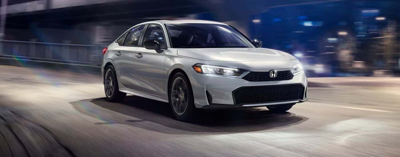 White 2026 Honda Civic driving on a city road at night.