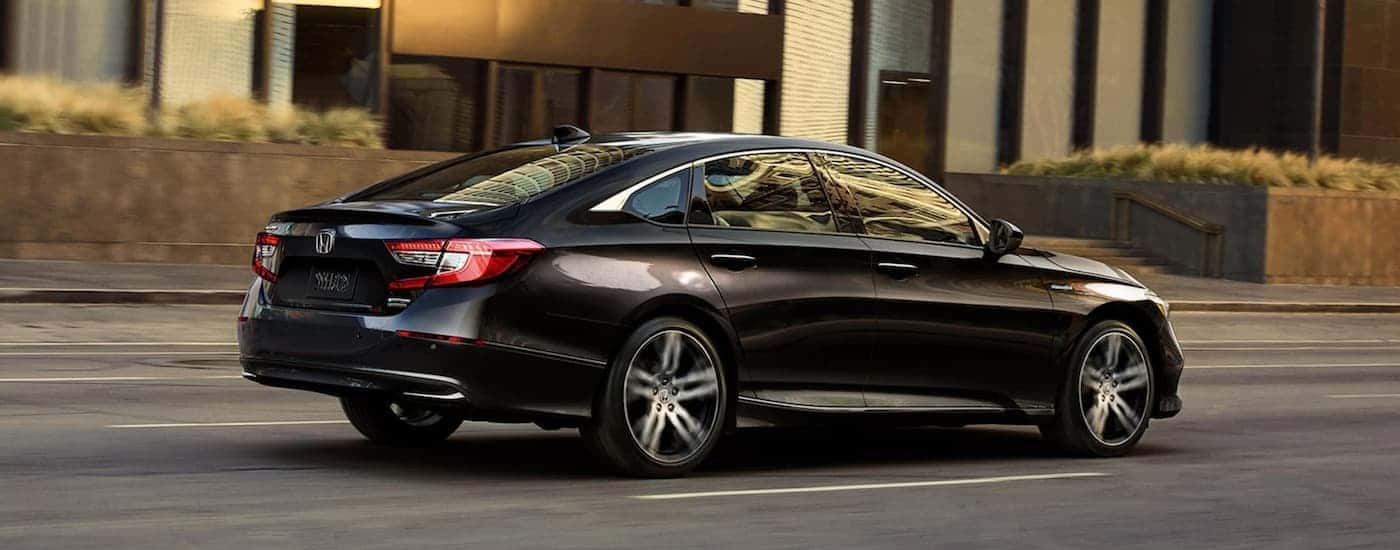A black 2021 Honda Accord Hybrid driving by a building.