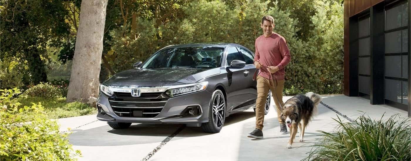 A gray 2021 Honda Accord Hybrid parked by a man and dog.