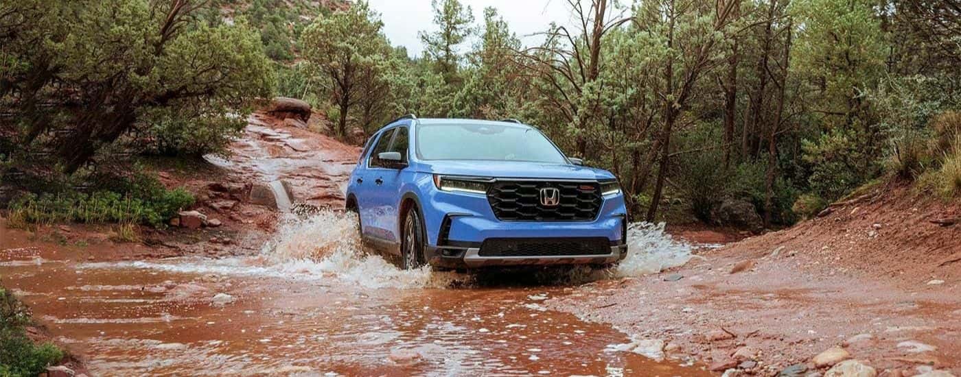 A blue 2023 Honda Pilot TrailSport driving through mud.