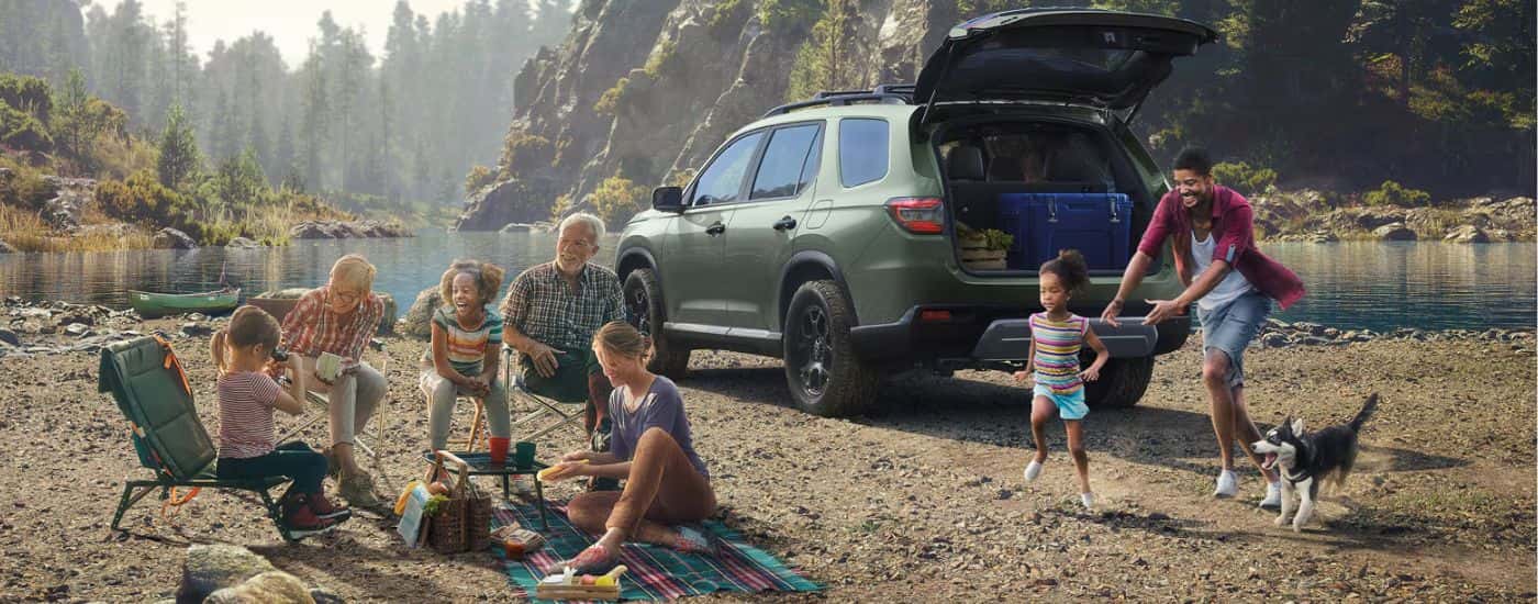Green 2026 Honda Pilot parked in front of a lake with a family.