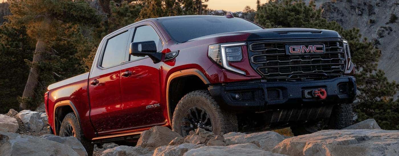 A red 2023 GMC Sierra 1500 ATX4 is shown off-roading on a rocky trail.