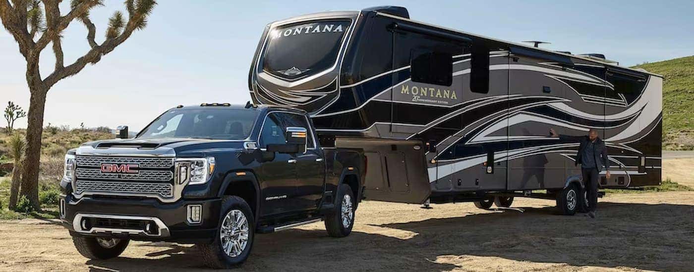 A black 2023 GMC Sierra 2500 HD Denali Ultimate is shown towing a large camper trailer.