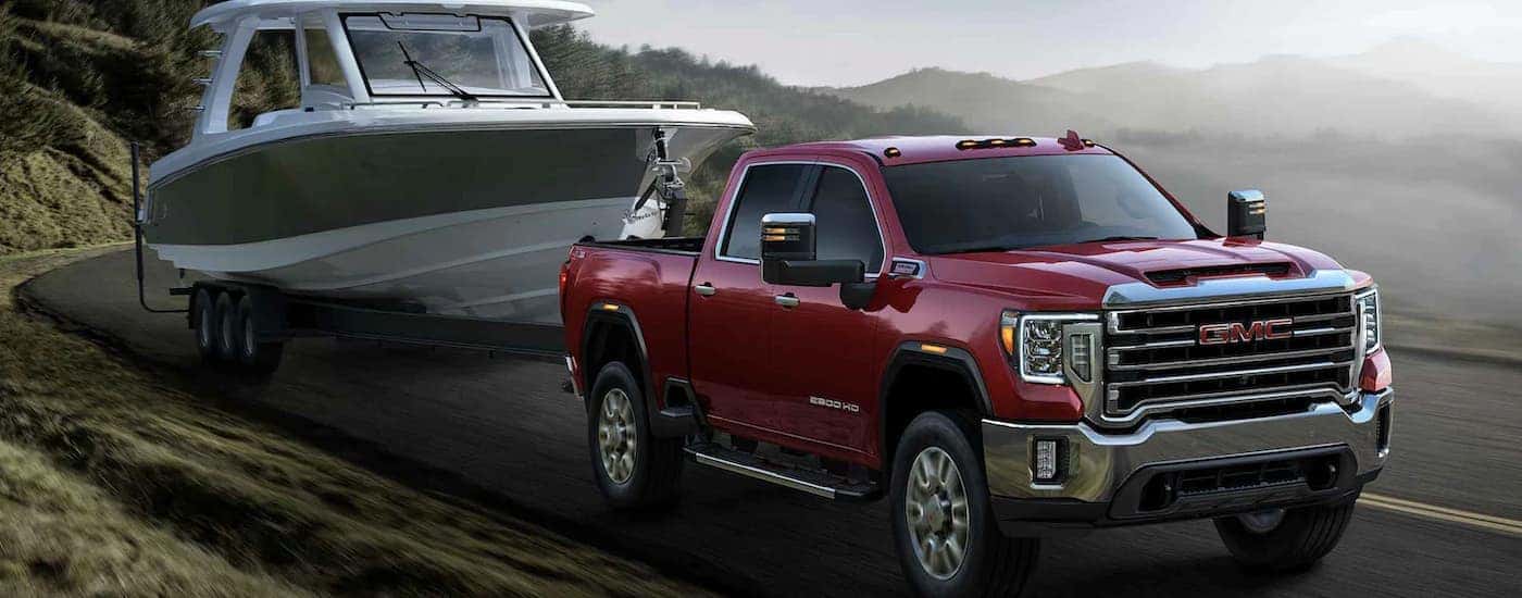 A red 2023 GMC Sierra 2500 HD is shown towing a boat on a foggy road.