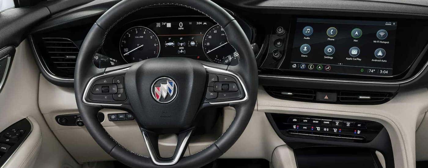 The black and white interior of a 2023 Buick Envision shows the steering wheel and infotainment screen.
