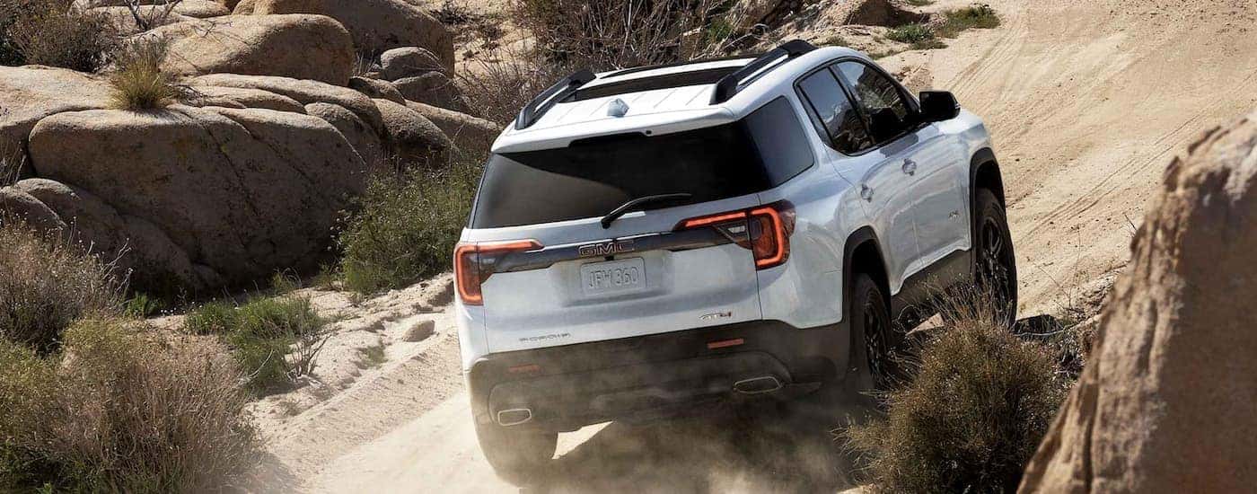 A white 2023 GMC Acadia AT4 is shown driving on dusty dirt road.