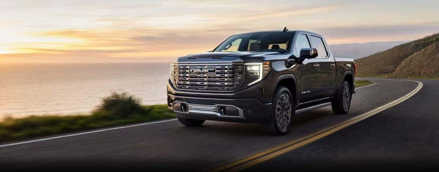 A gray 2024 GMC Sierra 1500 is shown driving on a highway near an ocean.