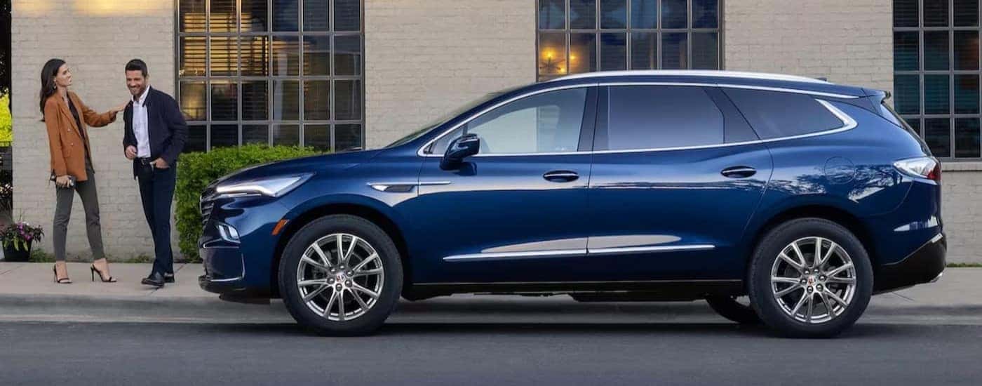A blue 2023 Buick Enclave is shown parked near two people.