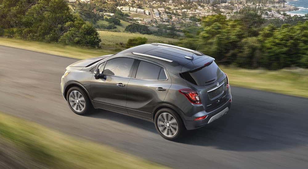 A gray 2017 Buick Encore is shown driving on a road near a city.
