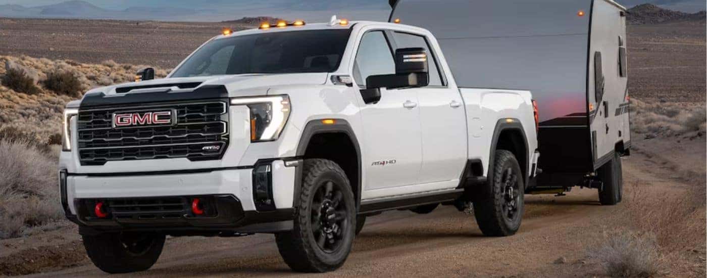 A white 2024 GMC Sierra 2500HD AT4 is shown towing a trailer.