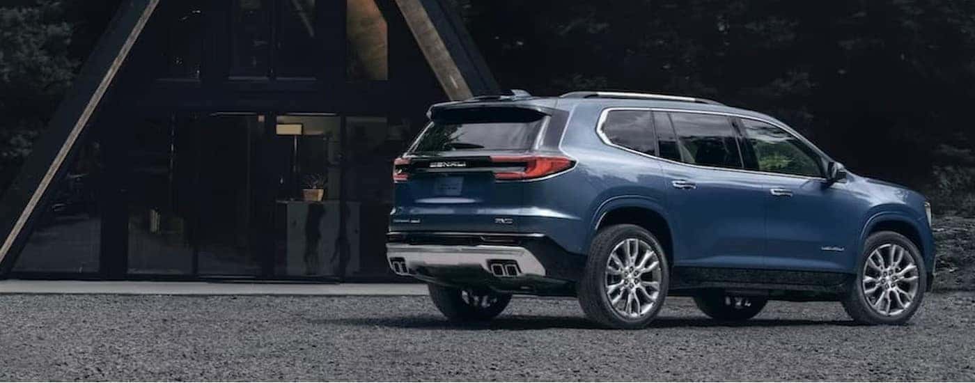 A blue 2024 GMC Acadia Denali is shown parked near an A-frame house.