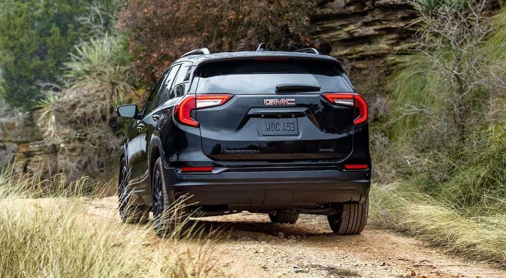 A rear view of a black 2024 GMC Terrain driving off-road on a dirt road.