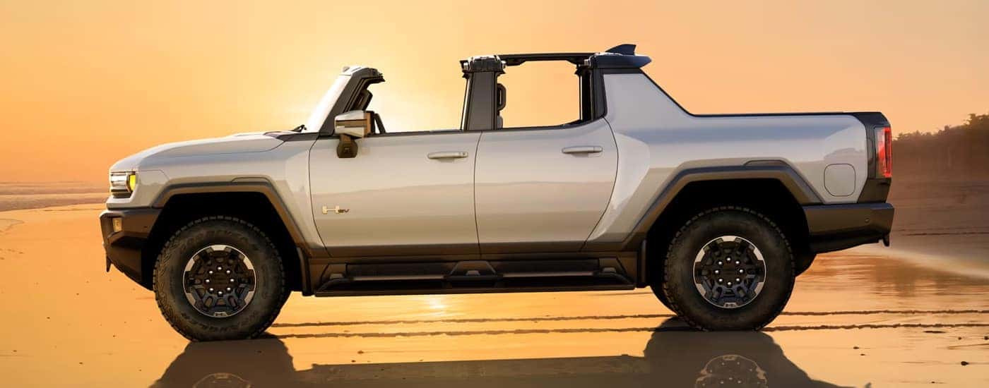 Side view of a silver 2024 GMC Hummer EV Pickup driving on the beach at sunset.