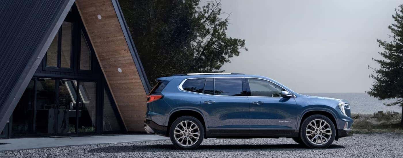 Side view of a blue 2024 GMC Acadia Denali parked next to an A-frame cabin.