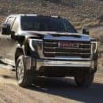 A black 2024 GMC Sierra 2500 HD Pro driving off-road on a trail.