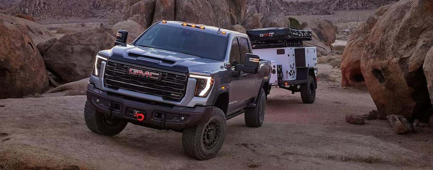 A gray 2025 GMC Sierra 2500 AT4X is shown towing a trailer off-road.