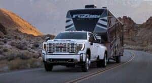 A popular GMC Denali, a white 2025 GMC 3500 HD Denali, is shown towing a trailer.