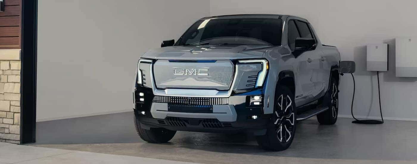 A silver 2025 GMC Sierra EV is shown charging in a garage.
