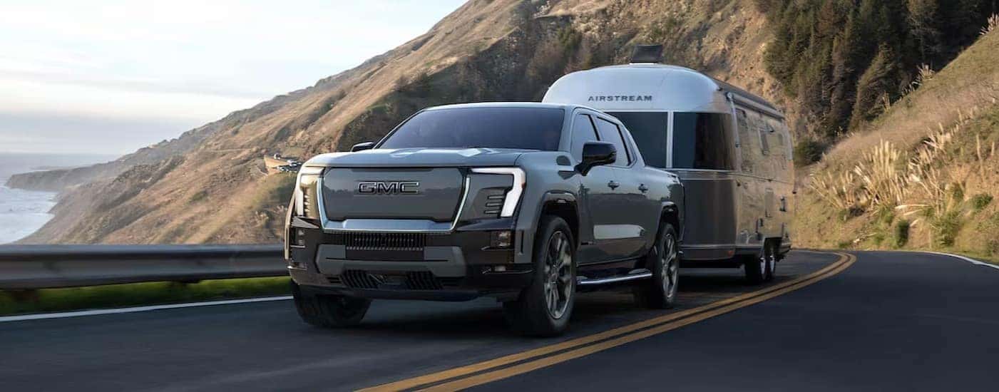 A silver 2025 GMC Sierra EV is shown towing a trailer on a highway.