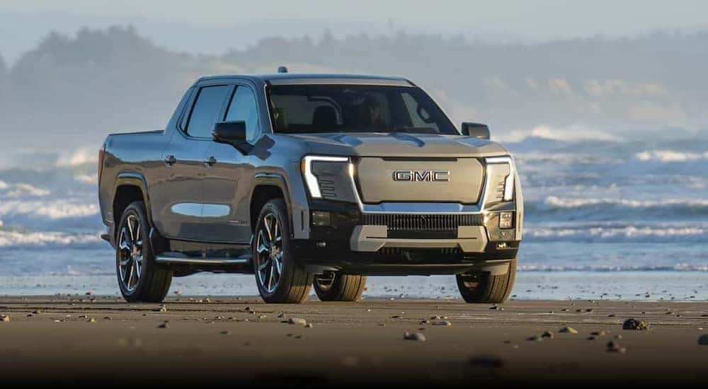 A silver 2025 GMC Sierra EV Denali is shown parked on a beach after viewing a GMC Sierra for sale.
