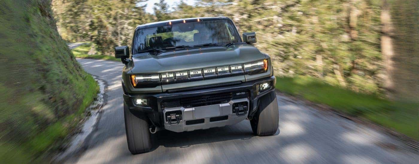A green 2024 GMC Hummer EV driving down a rural road