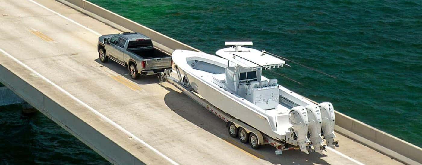 A silver 2025 GMC Sierra 2500 HD Denali towing a boat on a bridge.