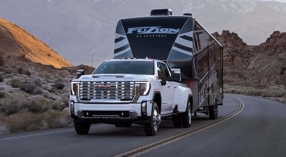 A white 2025 GMC Sierra 2500 HD Denali towing a trailer.