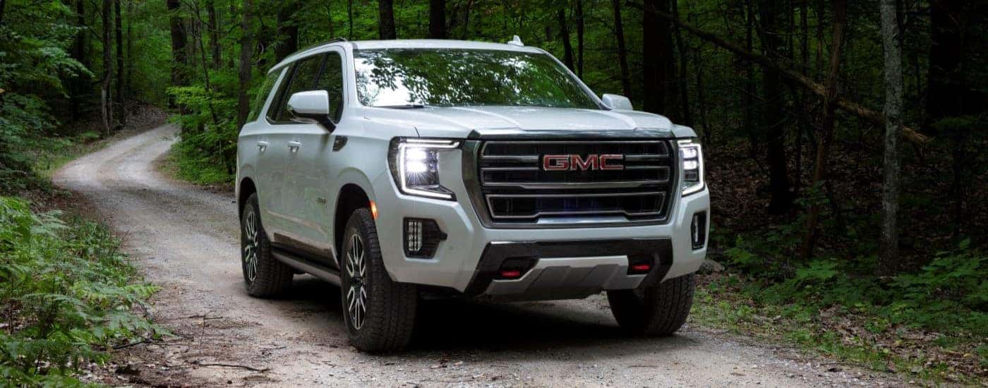 A white 2021 GMC Yukon AT4 is shown driving on a dirt trail in the woods.