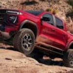 Red 2025 GMC Canyon driving up rocks.