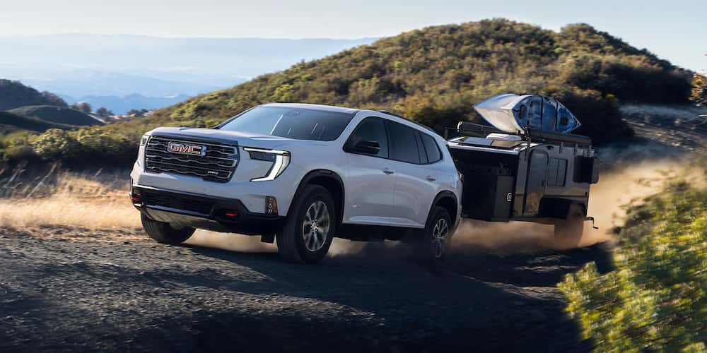 White 2026 GMC Acadia for sale towing cargo up a mountain.