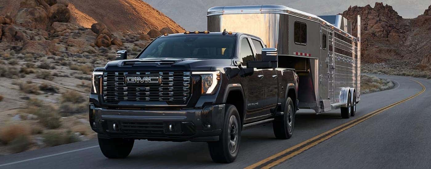 A black 2024 GMC Sierra 2500 Denali is shown towing a trailer to a GMC dealer near Johns Creek.