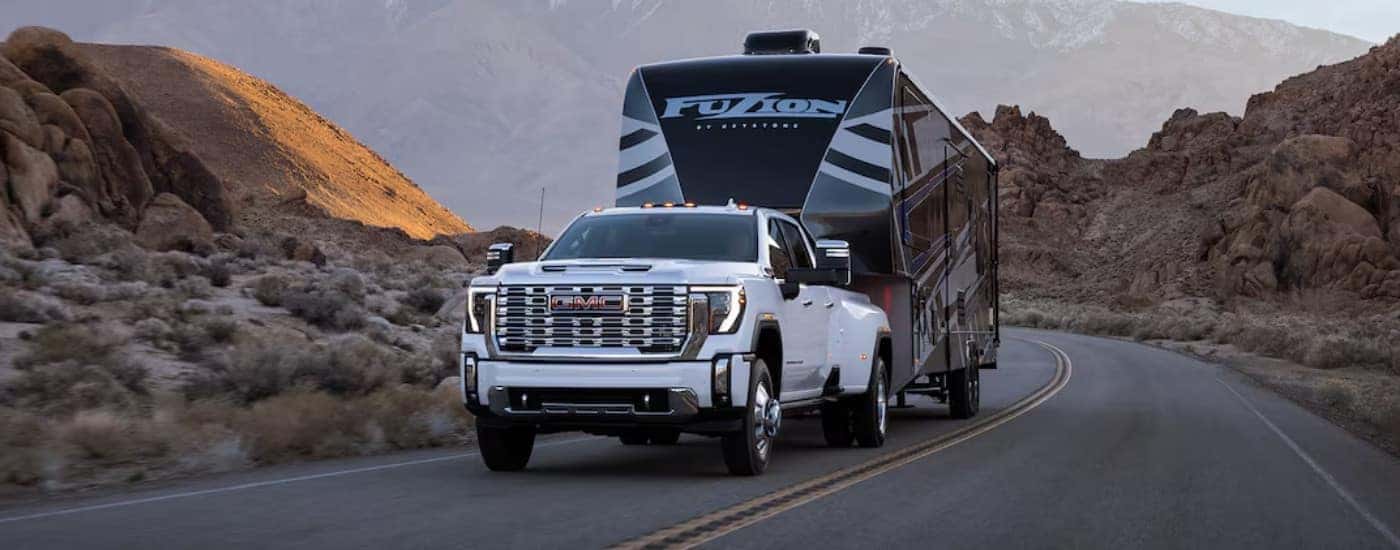 A popular GMC Denali, a white 2025 GMC 3500 HD Denali, is shown towing a trailer.