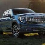 Blue 2026 GMC Sierra 1500 driving up a grass hill.