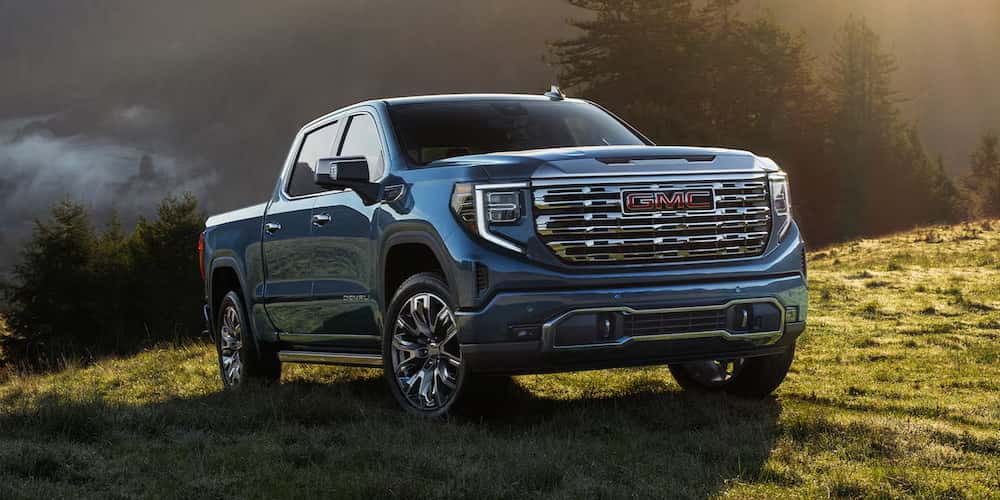 Blue 2026 GMC Sierra 1500 driving up a grass hill.
