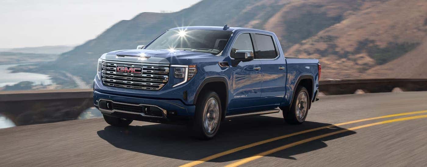 Blue 2025 GMC Sierra 1500 Denali driving around a bend.