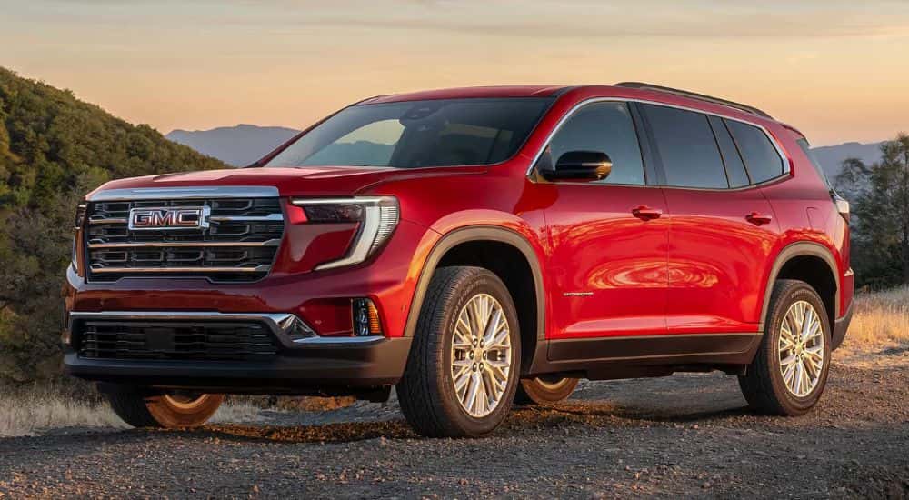 Red 2026 GMC Acadia parked on a dirt trail.