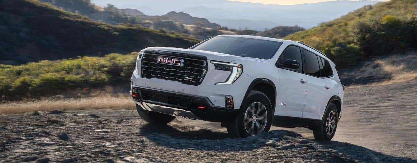 White 2026 GMC Acadia AT4 driving up rocks.